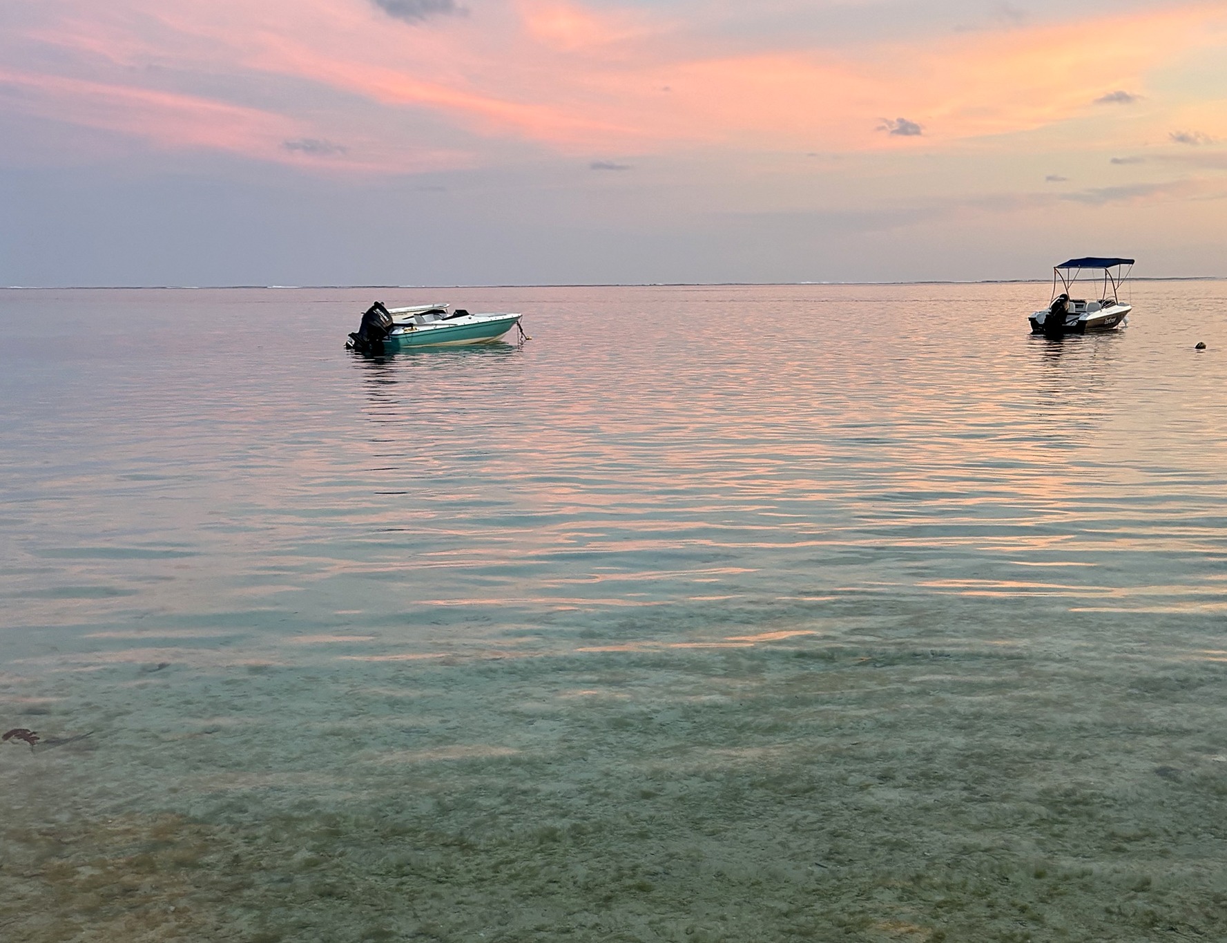Mer calme au coucher du soleil, deux petits bateaux à l'ancre et des reflets roses sur l'eau